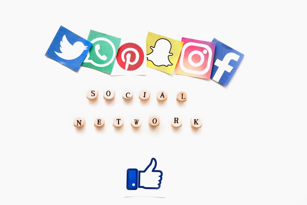 Image showing icons for different social media networks including Twitter, WhatsApp, Pinterest, Snapchat, Instagram, and Facebook arranged in a row at the top. Underneath is the text "SOCIAL NETWORK" spelled out with wooden letter tiles. A 'thumbs up' icon is at the bottom.