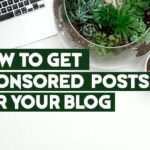 Image showing a white desk with a laptop, eyeglasses, a camera lens, and various potted plants, including succulents and cacti. The text on the image reads "HOW TO GET SPONSORED POSTS FOR YOUR BLOG" in bold green lettering.