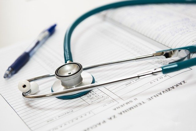 A stethoscope rests on top of a medical document with printed text, alongside a blue pen. The scene suggests a medical or healthcare setting, focusing on patient care or record-keeping.