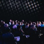 crowd of people sitting on chairs inside room, hybrid event