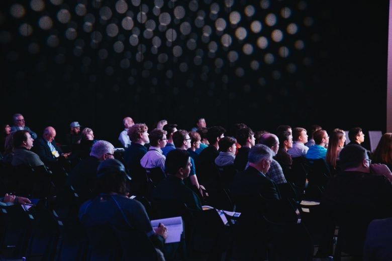 crowd of people sitting on chairs inside room, hybrid event