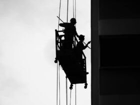 Black and White Photo of Men Working on a Hanging Platform, Painting Perfection