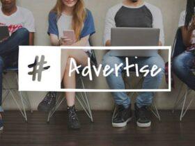 Four young adults sit in a row, using various devices like smartphones and a laptop. An overlay text reads "#Advertise," implying a focus on digital media or marketing. They are casually dressed and seated against a plain wall with a wooden floor.