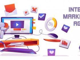 Illustration of a computer desk with a monitor displaying a play button, surrounded by digital marketing symbols such as a megaphone, percentage chart, thumbs-up, and notification icons. Text on the right reads "Internet Marketing Agency.