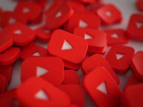 A pile of red YouTube play button icons, each featuring the familiar white play triangle in the center. The buttons are scattered randomly, creating a dense and vibrant pattern that represents the popular video-sharing platform.