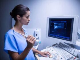 Woman in blue scrubs using an ultrasound machine, looking at the screen displaying an image.