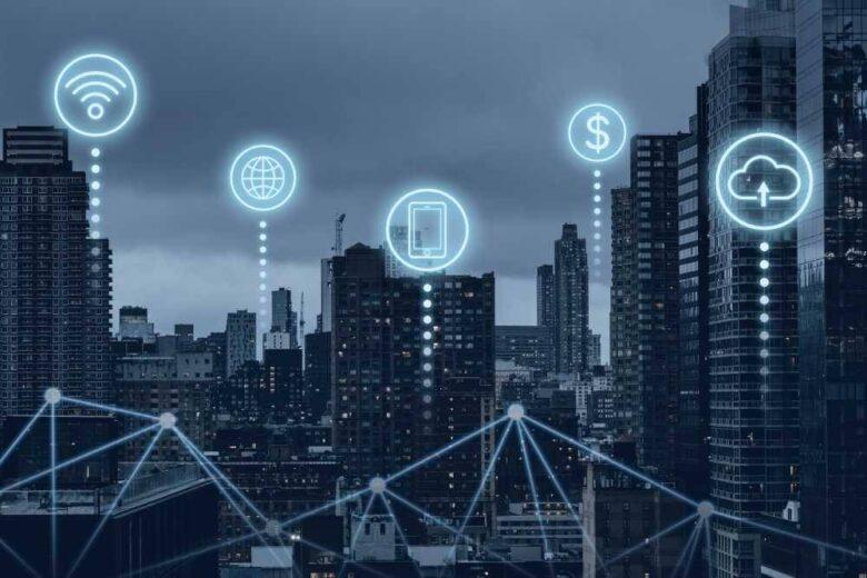 A cityscape at dusk with glowing technology icons overlaid, representing Wi-Fi, internet, smartphones, finance, and cloud computing. The icons are connected by dotted lines, symbolizing interconnected digital infrastructure in an urban environment.
