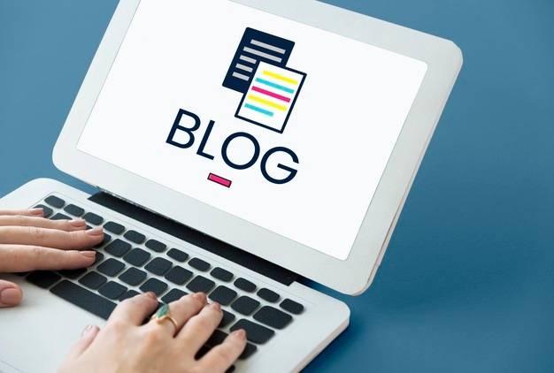 A person types on a laptop displaying the word "BLOG" in bold letters on the screen, accompanied by an icon of two overlapping documents. The background is a plain blue surface.