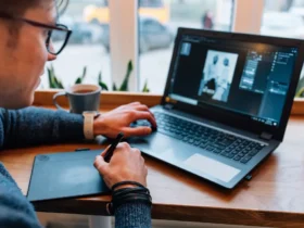 man is editing photos on laptop, using graphics tablet and interactive pen display