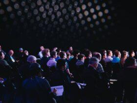 crowd of people sitting on chairs inside room, hybrid event