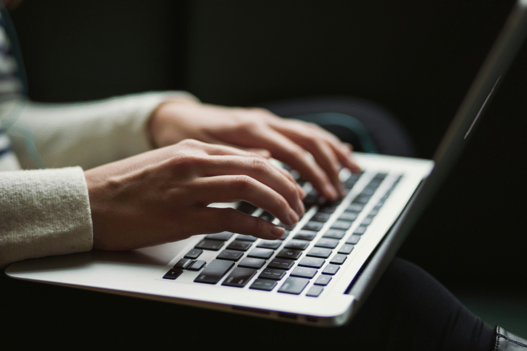 Close-up of a person typing on a laptop keyboard, showing hands in focus on the keys with a dark blurred background.