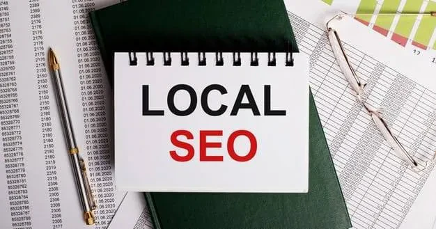 A notepad with "LOCAL SEO" written on it is placed on top of several documents with numbers. A pair of glasses and a pen are nearby.