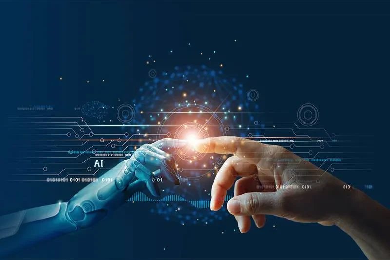A human hand and a robotic hand reach out to touch fingertips against a dark background filled with digital circuitry and binary code. A glowing orb at their point of contact symbolizes connection or collaboration between humans and artificial intelligence.