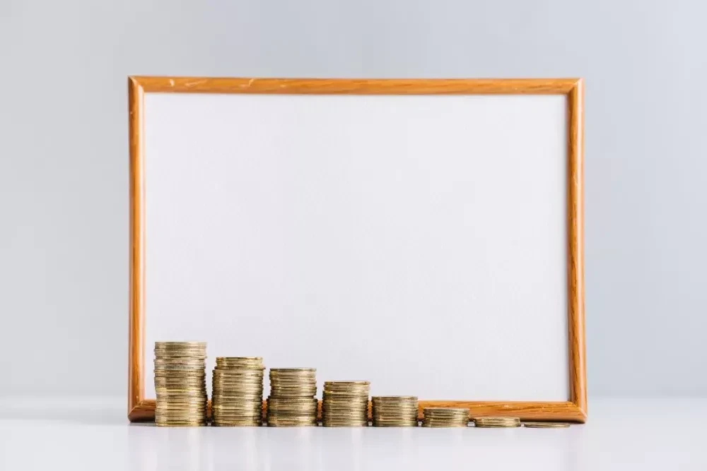 increasing stacked gold coins in front of blank white board on reflective desk