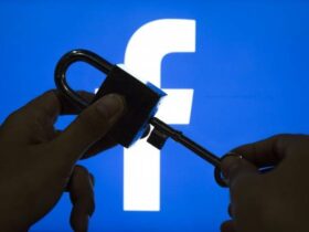 A pair of hands is holding a padlock and key in front of a large, illuminated Facebook logo. One hand is holding the padlock, while the other is inserting the key into the lock, suggesting the idea of unlocking or accessing Facebook.