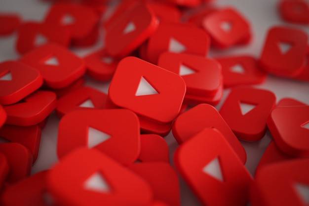 A pile of red YouTube play button icons, each featuring the familiar white play triangle in the center. The buttons are scattered randomly, creating a dense and vibrant pattern that represents the popular video-sharing platform.