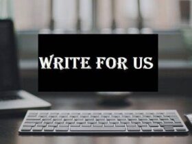 A sleek white keyboard is situated on a dark desk with a blurred background of a window and a computer screen. In the center of the image, a black rectangle with white text reads "WRITE FOR US" in bold, stylized font.