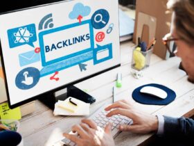 A person types on a keyboard at a desk with a computer screen displaying the word "BACKLINKS" surrounded by various icons like a cloud, email, link, and share symbol, indicating internet and digital communication themes. The workspace is bright and organized.