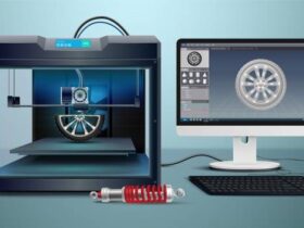 A 3D printer is producing a wheel design, as shown on a computer monitor next to it. A detailed rendering of the wheel is displayed on the monitor's screen. In front of the 3D printer and monitor, a red and silver mechanical component rests on the desk.